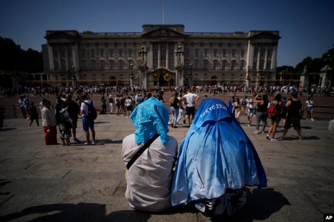 People sit covering their heads from the sun after a scaled down version of the Changing of the Guard ceremony took place outside Buckingham Palace, during hot weather in London, Monday, July 18, 2022. (AP Photo/Matt Dunham)