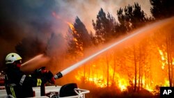 Esta fotografía proporcionada el viernes 15 de julio de 2022 por la brigada de la región de Gironde, muestra a unos bomberos usando una manguera para contener un incendio forestal cerca de Landiras, en el suroeste de Francia, el jueves 14 de julio de 2022. (SDIS 33 via AP)