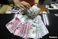 Seorang teller di money changer menampilkan Rupiah Indonesia dan dolar AS di Jakarta, 12 Agustus 2015. (REUTERS/Rivan Awal Lingga/Antara)