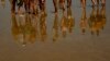FILE - People's images are reflected on the water while walking along the beach in Laredo, northern, Spain, July 18, 2022.