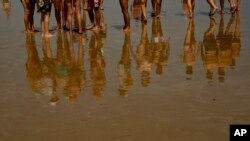 FILE - People's images are reflected on the water while walking along the beach in Laredo, northern, Spain, July 18, 2022.