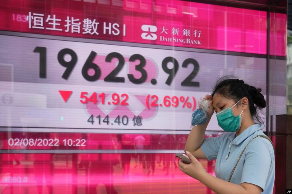 週二香港街頭，一名女子走過恆生指數顯示大跌的電子顯示牌。 （2022年8月2日）