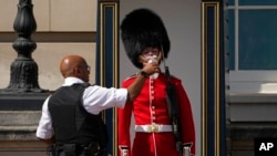 FILE - A police officer givers water to a British soldier wearing a traditional bearskin hat, on guard duty outside Buckingham Palace, during hot weather in London, July 18, 2022.