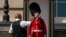 FILE - A police officer givers water to a British soldier wearing a traditional bearskin hat, on guard duty outside Buckingham Palace, during hot weather in London, July 18, 2022.