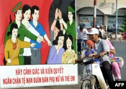 Sebuah keluarga melewati poster yang mengimbau masyarakat untuk waspada dan bertekad melawan praktik perdagangan manusia, di sebuah jalan di Kota Ho Chi Minh, 24 Februari 2003. (Foto: AFP)