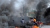 Sejumlah pengendara motor melewati penghalang jalan yang sengaja dibakar dalam konflik antara geng di Port-au-Prince, Haiti, 13 Juli 2022. (Foto: Ralph Tedy Erol/Reuters)