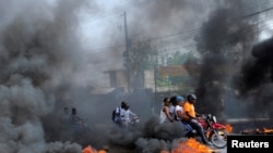 FILE - Motorcycle drivers pass through a burning road block as anger mounted over fuel shortages that have intensified as a result of gang violence, in Port-au-Prince, Haiti, July 13, 2022.