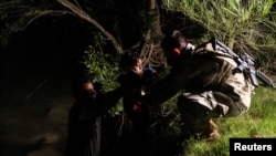 Un traficante de personas pasa a un niño migrante que busca asilo a un miembro de la Guardia Nacional de los EEUU después de cruzar el río Grande hacia los Estados Unidos desde México en Roma, EEUU, el 10 de junio de 2021.