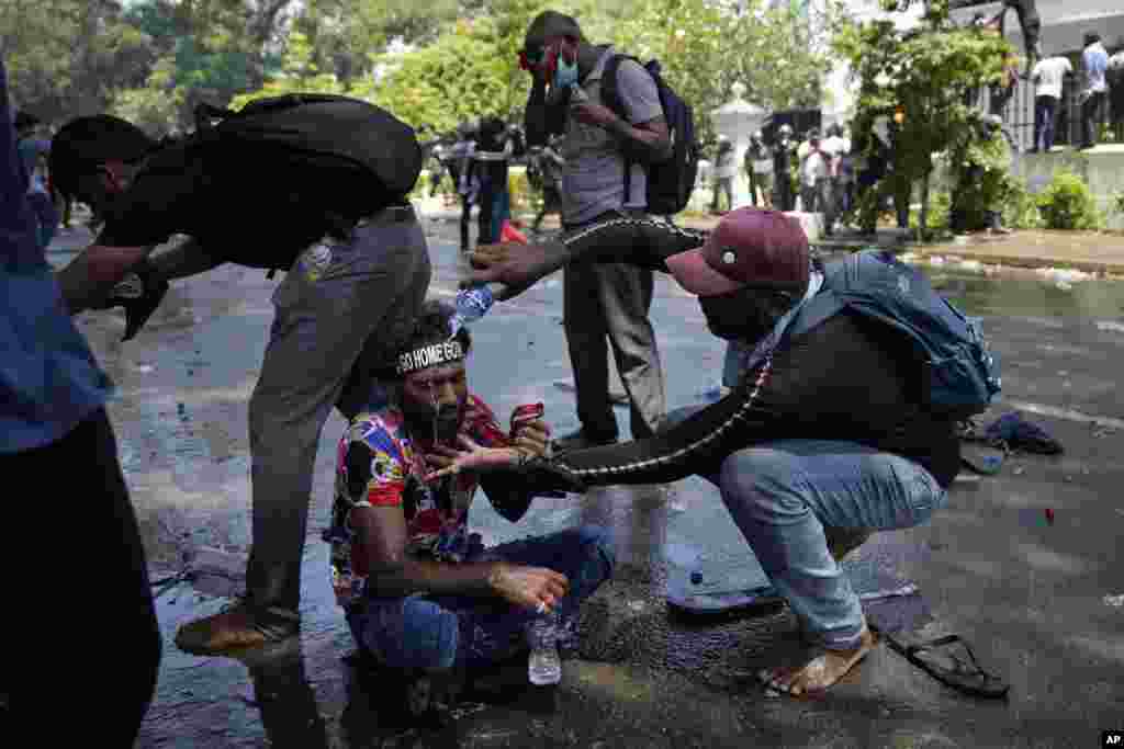 A protester helps another after police fired teargas to disperse them before they stormed Prime Minister Ranil Wickremesinghe&#39;s office in Colombo, July 13, 2022.