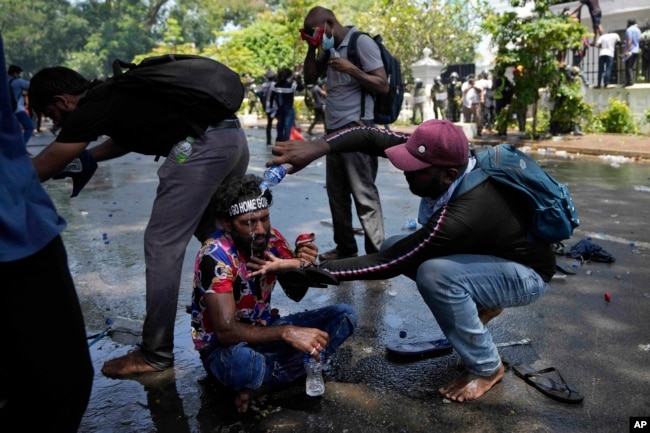 A protester helps another after police fired teargas to disperse them before they stormed Sri Lankan Prime Minister Ranil Wickremesinghe's office on July 13, 2022. (AP Photo/Eranga Jayawardena)