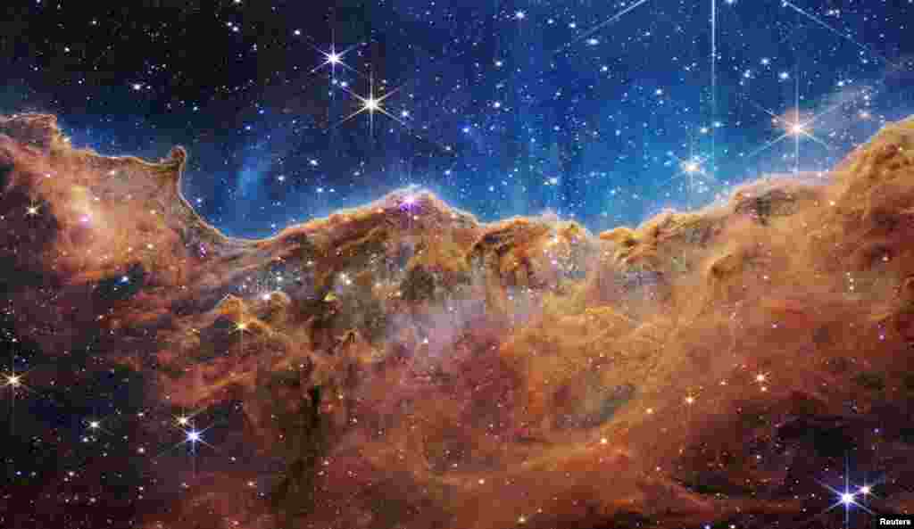 The &quot;Cosmic Cliffs&quot; of the Carina Nebula are seen in an image divided horizontally by an undulating line between a cloudscape forming a nebula along the bottom portion and a comparatively clear upper portion, with data from NASA&#39;s James Webb Space Telescope, released July 12, 2022.