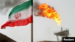 FILE - FILE - A gas flare on an oil production platform is seen alongside an Iranian flag in the Gulf.