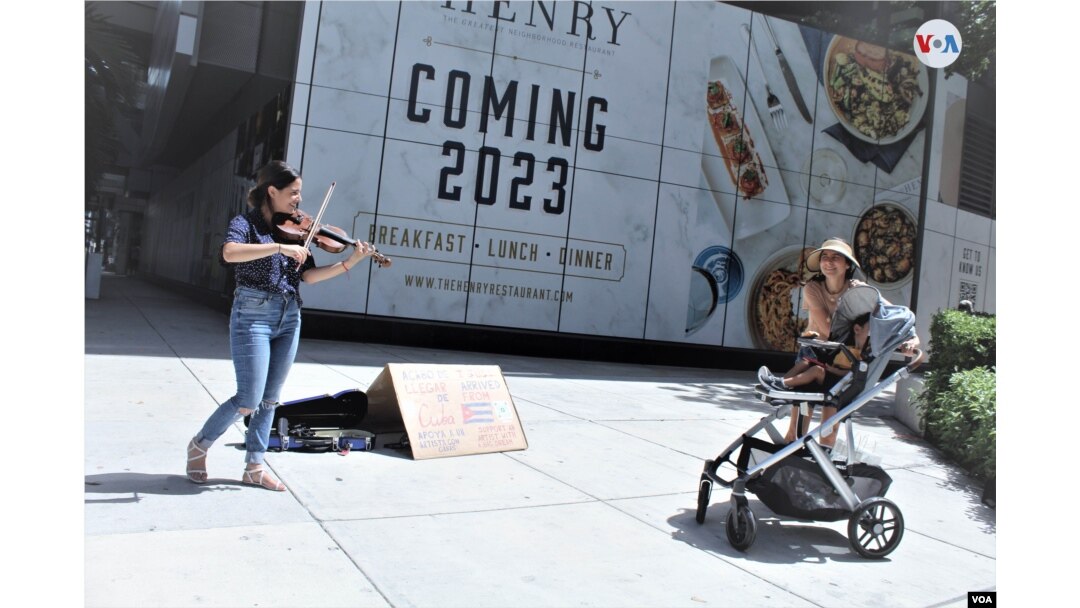 Una mujer con su hijo se detiene a escuchar la interpretación que hace al violín la cubana Olivia De Armas en una calle de Miami, EEUU, el 21 de julio de 2022. Foto: Luis F. Rojas, VOA.