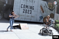 Una mujer con su hijo se detiene a escuchar la interpretación que hace al violín la cubana Olivia De Armas en una calle de Miami, EEUU, el 21 de julio de 2022. Foto: Luis F. Rojas, VOA.