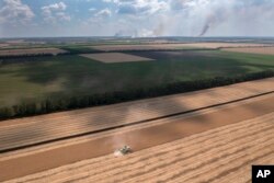 Smoke rises in the background during a fierce battle on the frontline, as a farmer collects harvest in a field in the Dnipropetrovsk region, Ukraine, July 4, 2022.