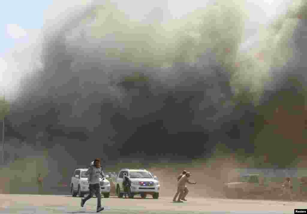 People run as dust rises after explosions hit Aden Airport upon the arrival of members of the newly-formed Yemeni government, in Aden.