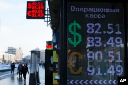 FILE - People walk past an exchange office screen showing the currency exchange rates of the Russian ruble, U.S. dollar and euro in Moscow, Jan. 21, 2016.