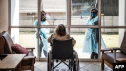ARCHIVO - Familiares conversan por una ventana con una mujer en silla de ruedas, una residente de Casa Serena, un hogar de ancianos, en Johannesburgo, África del Sur, el 22 de julio de 2020..