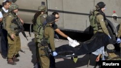 以色列军人抬着一具巴勒斯坦人的尸体，以色列警方说，这名巴勒斯坦人在持刀行凶后被击毙。(2015年10月29日)