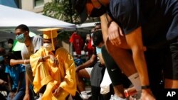 Brian Gardener, left, wears his middle school graduation cap and gown as he kneels with demonstrators in remembrance of George Floyd, June 13, 2020, near the White House in Washington. 