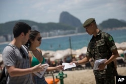 An army soldier distributes a pamphlet about the Aedes aegypti mosquito that spreads the Zika virus on the edge of the Copacabana beach, in Rio de Janeiro, Feb. 13, 2016.