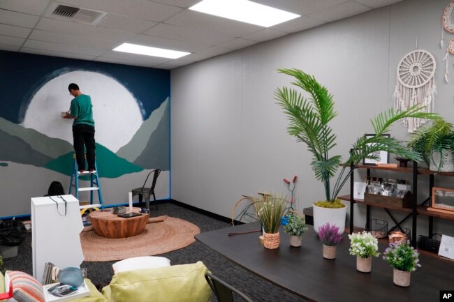 A man paints a mural of a giant moon over mountains during construction of University High School's Well Space in Irvine, Calif., on July 28, 2022. When school starts, the room is to be staffed full-time with a counselor or mental health specialist. (AP Photo/Eugene Garcia)