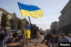 A boy waves a national flag atop of armored personal carrier at an exhibition of destroyed Russian military vehicles and weapons, dedicated to the upcoming country's Independence Day, amid Russia's attack on Ukraine, in the center of Kyiv, Aug. 21, 2022.