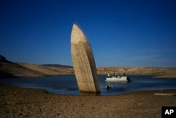 FILE - A formerly sunken boat points upright into the air with its stern stuck in the mud along the shoreline of Lake Mead at the Lake Mead National Recreation Area, near Boulder City, Nevada, June 10, 2022.