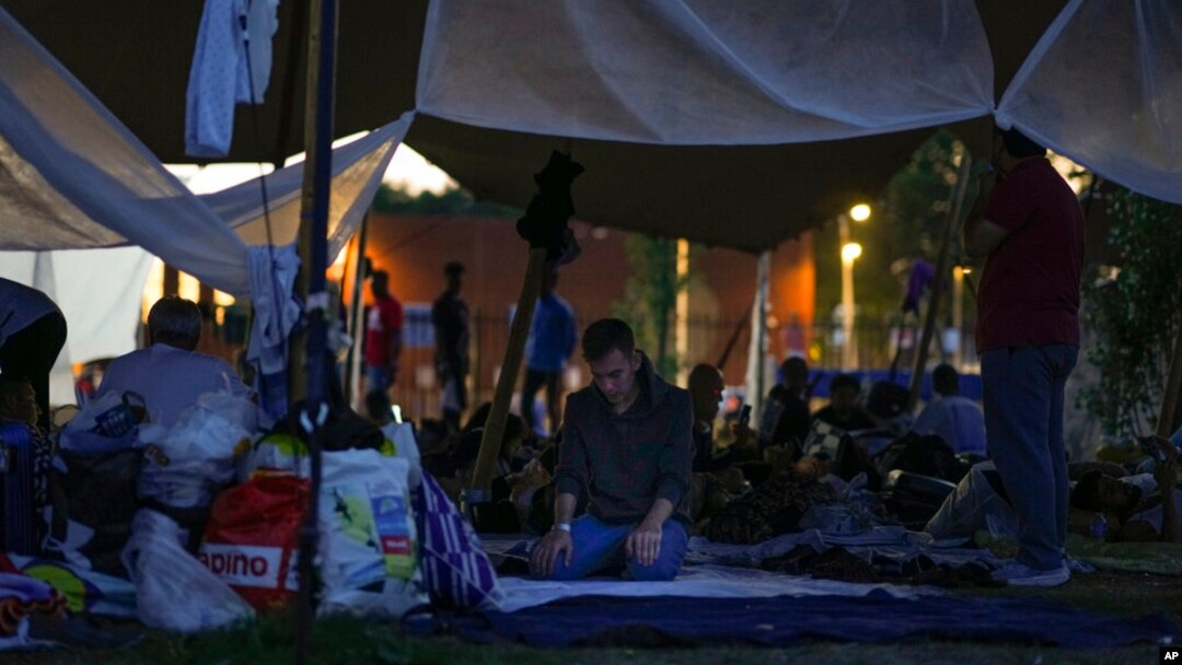 A man prays under a tarpaulin as hundreds of migrants who seek shelter prepared to spend the night outside an overcrowded asylum seekers center in Ter Apel, northern Netherlands, Aug. 25, 2022.