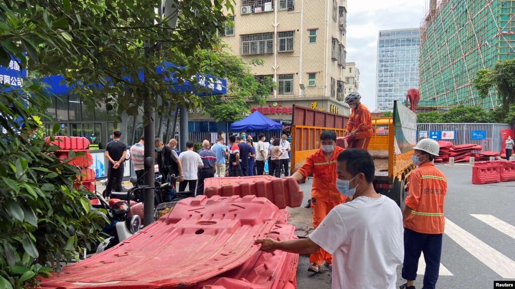 中国广东深圳的工人正在准备给一住宅小区外竖立围栏，与此同时小区居民正在排队做核酸。（2022年8月29日）(photo:VOA)