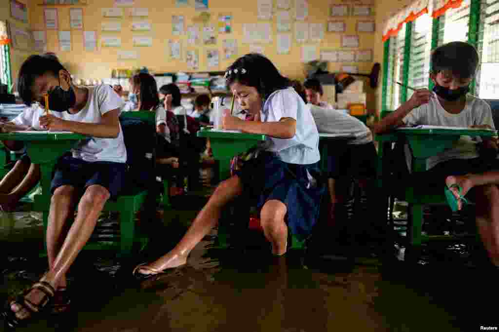 Alunos frequentam o primeiro dia de aulas presenciais, numa escola inundada devido à maré alta, em Macabebe, província de Pampanga, Filipinas, 22 de Agosto de 2022.