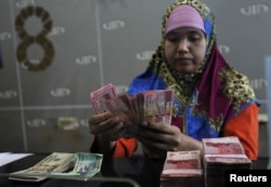 ILLUSTRATION - A bank teller counts rupiah banknotes for his customers in Jakarta, August 26 2015. (REUTERS/Nyimas Laula)