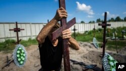 A funeral worker installs a cross with a number plate on the grave of an unidentified civilian killed by Russian troops during the Russian occupation in Bucha near Kyiv, Ukraine. Twenty-one unidentified bodies exhumed from a mass grave were buried in Bucha on Wednesday. (AP Photo/Evgeniy Maloletka)