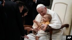 Pope Francis cradles a child on his lap at the end of his weekly general audience in the Paul VI Hall at The Vatican.