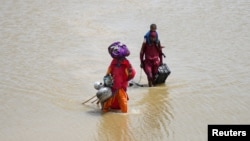 Members of a family with their belongings wade through water following heavy rain and flooding during the monsoon season in Jamshoro, Pakistan Aug. 26, 2022.