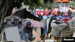 A homeless man prepares food as marchers pass by after the members of several labor unions began a nationwide strike over the high cost of living in Cape Town, South Africa.