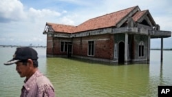 FILE - A man walks past a house abandoned after it was inundated by water due to the rising sea level in Sidogemah, Central Java, Indonesia, Nov. 8, 2021. Climate hazards such as flooding, heat waves and drought have worsened known infectious diseases in people. (AP Photo)