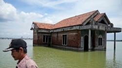 Seorang warga berjalan melewati sebuah rumah yang kini terendam akibat naiknya permukaan air laut di Sidogemah, Demak, Jawa Tengah, pada 8 November 2021. (Foto: AP/dita Alangkara)