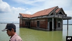 Seorang warga berjalan melewati sebuah rumah yang kini terendam akibat naiknya permukaan air laut di Sidogemah, Demak, Jawa Tengah, pada 8 November 2021. (Foto: AP/dita Alangkara)