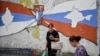 Kosovo Serbs walk next to a mural reading "Kosovo is Serbia and Crimea is Russia" in the Serb majority north of Mitrovica, Aug. 26, 2022.