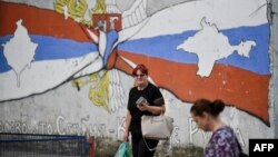 Kosovo Serbs walk next to a mural reading "Kosovo is Serbia and Crimea is Russia" in the Serb majority north of Mitrovica, Aug. 26, 2022.