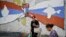 Kosovo Serbs walk next to a mural reading "Kosovo is Serbia and Crimea is Russia" in the Serb majority north of Mitrovica, Aug. 26, 2022.