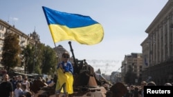 FILE - A boy waves a national flag atop of armored personal carrier at an exhibition of destroyed Russian military vehicles and weapons, dedicated to the upcoming country's Independence Day, amid Russia's attack on Ukraine, in the center of Kyiv, Ukraine, Aug. 21, 2022. 