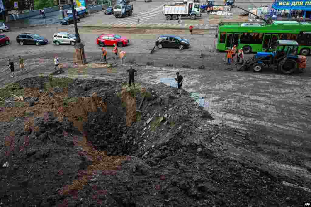 Municipal service workers stand near a crater near the damaged headquarters of the Kharkiv administration building following an overnight Russian missile strike in Kharkiv, Ukraine.