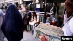 FILE - A person holds a bundle of Afghan afghani banknotes at a money exchange market, following banks and markets reopening after the Taliban took over in Kabul, Afghanistan, Sept. 4, 2021. 