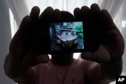 A Cuban migrant, who wished not to be identified for fear of reprisals against his family back on the island nation, holds up a picture of a home-made boat that brought him and three others to the U.S., Tuesday, June 21, 2022. (AP Photo/Wilfredo Lee)