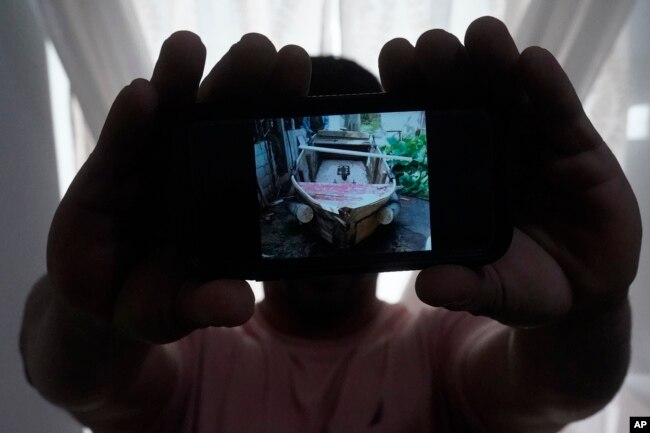 A Cuban migrant, who wished not to be identified for fear of reprisals against his family back on the island nation, holds up a picture of a home-made boat that brought him and three others to the U.S., Tuesday, June 21, 2022. (AP Photo/Wilfredo Lee)