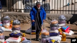 یک مرد افغان در میان بسته‌های غذایی که برای کمک‌ها به خانواده های نیازمند روی زمین چیده شده ایستاده است. کابل، افغانستان - ۱۶ فوریه ۲۰۲۲