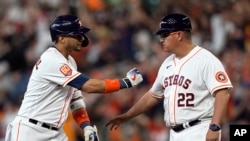 Yuli Gurriel (izquierda) de los Astros de Houston saluda al coach de primera base Omar López (22) tras batear un sencillo remolcador ante los Medias Rojas de Boston, el 2 de agosto de 2022. 