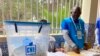 Delegado de mesa olha para urna com os boletins de voto, em Luanda, Angola